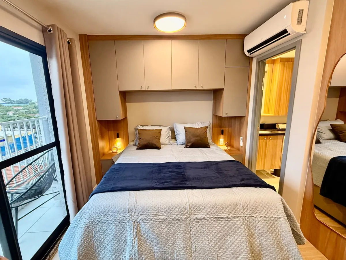 Studio no Alto da Boa Vista: cama arrumada com manta azul e janela