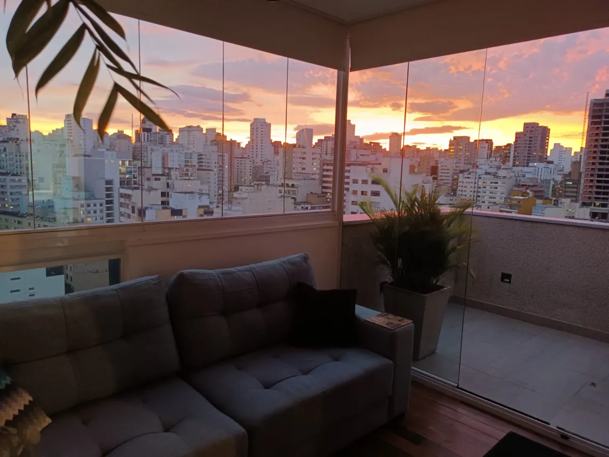 Varanda envidraçada do apartamento em Higienópolis ao pôr do sol, com vista para os prédios de São Paulo