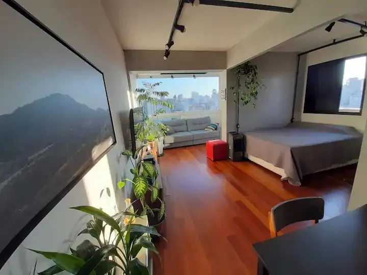 Sala do apartamento em Higienópolis com piso de madeira, plantas e vista para a cidade